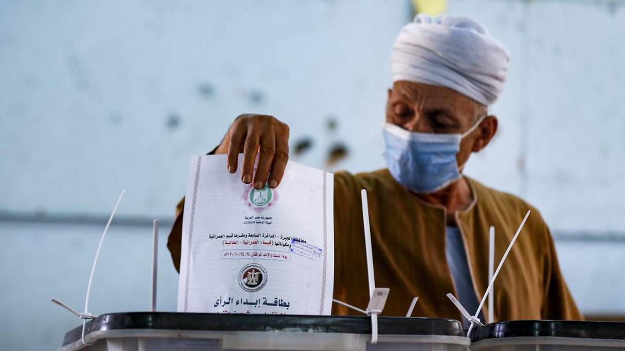 Un homme en masque glissant son bulletin dans l'urne dans un bureau de vote à Talibeya à Gizeh.