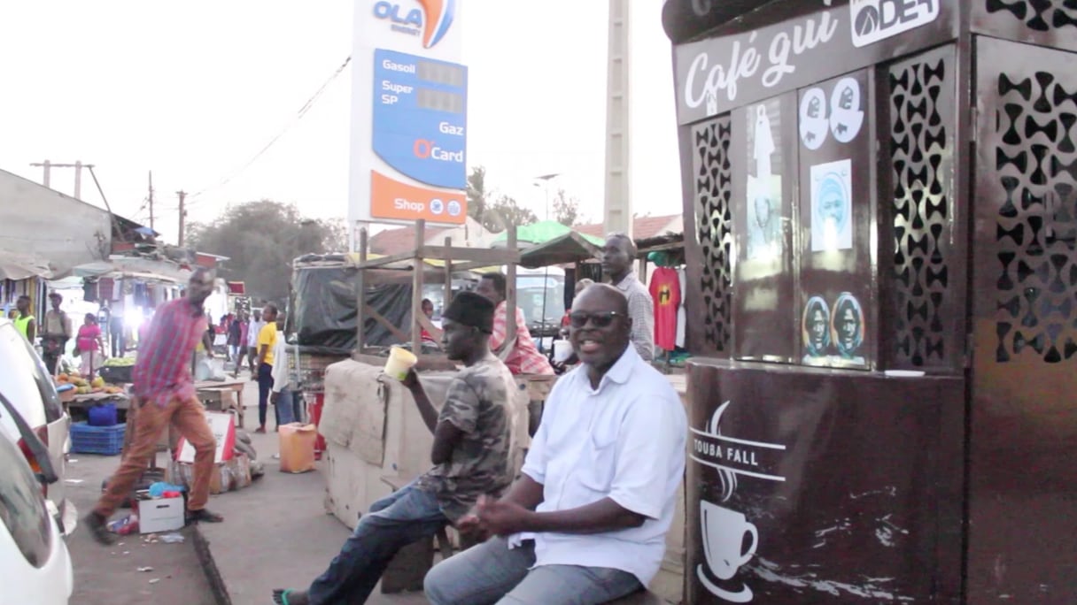 Des Dakarois assis à côté d'un vendeur de café de rue.