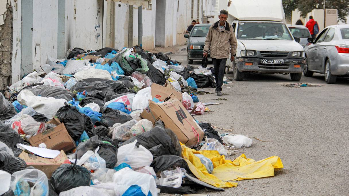 Un homme marche le long d'une rue devant des sacs et des cartons d'ordures empilés dans le centre de la ville côtière de Sfax, à environ 270 kilomètres au sud-est de la capitale tunisienne, le 6 novembre 2021.