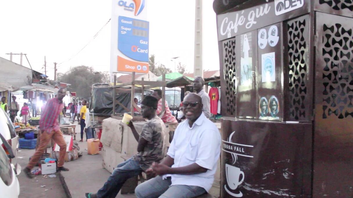 Des Dakarois assis à côté d'un vendeur de café de rue.