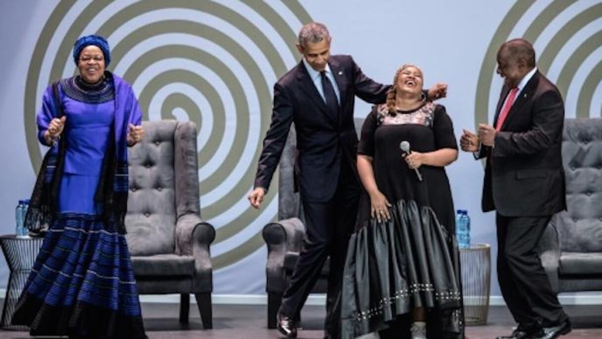 L'ex président américain Barack Obama, la veuve de Nelson Mandela, Graça Machel (à gauche) et le président sud-africain Cyril Ramaphosa (à droite) dansent en compagnie de la chanteuse Thandiswa Mazwai lors d'une cérémonie en l'honneur de Mandela, le 17 juillet 2018 à Johannesburg.