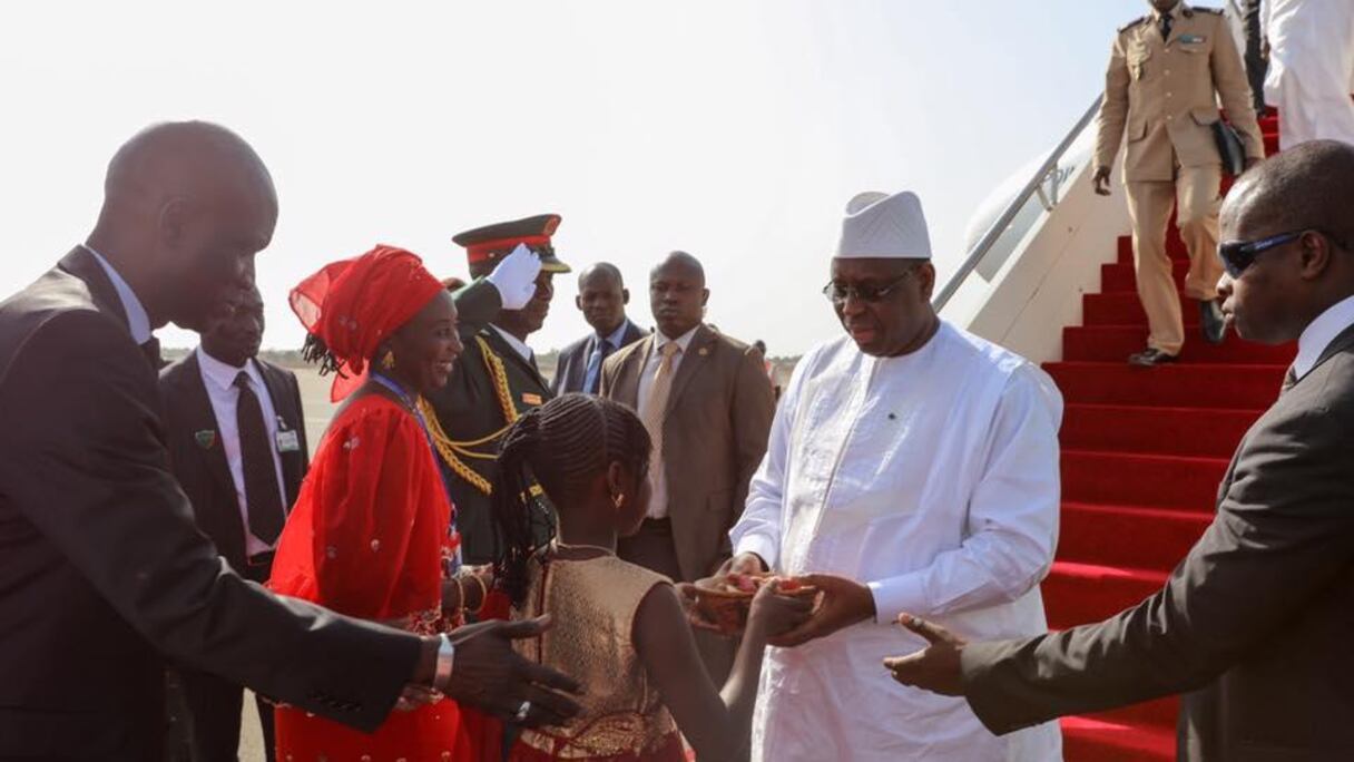 Macky Sall recevant une calebasse de fruits secs des mains d'une petite gambienne