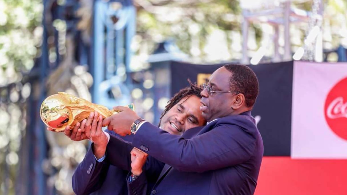 Visiblement, le président sénégalais et Chistian Karambeu veulent tout savoir de la Coupe du Monde, y compris le nom des vainqueurs. Le trophée porte l'inscription «FIFA World Cup» gravée à sa base. Le nom des vainqueurs sont gravés sur la base opposée du trophée. Le texte indique l'année et le nom de chaque nation championne du monde.