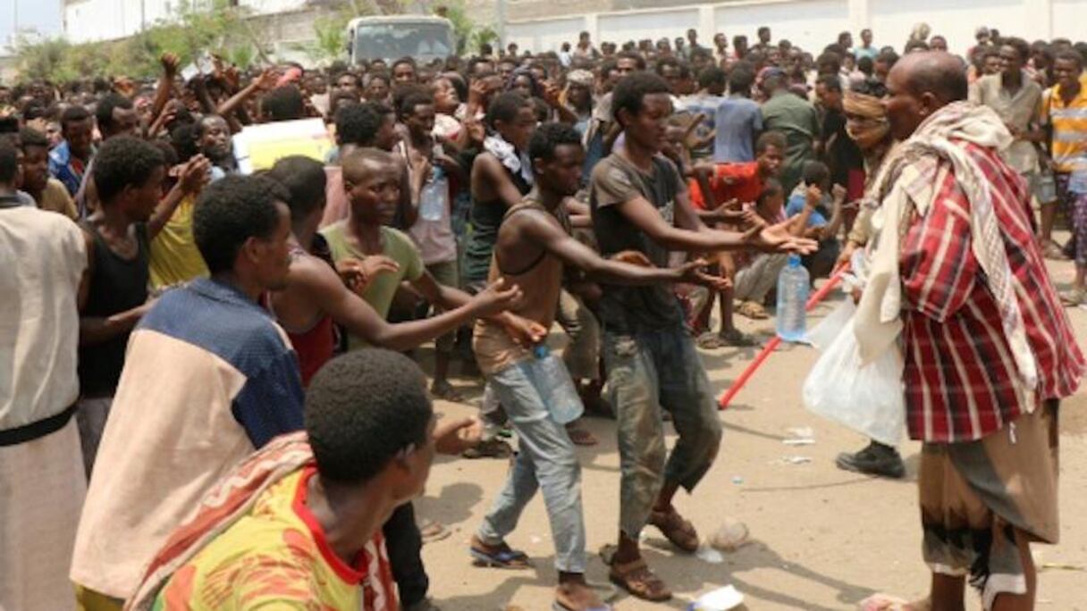 Des centaines de migrants tendent la main pour prendre une tranche de pain, ce 23 avril 2019, dans un stade à Aden.