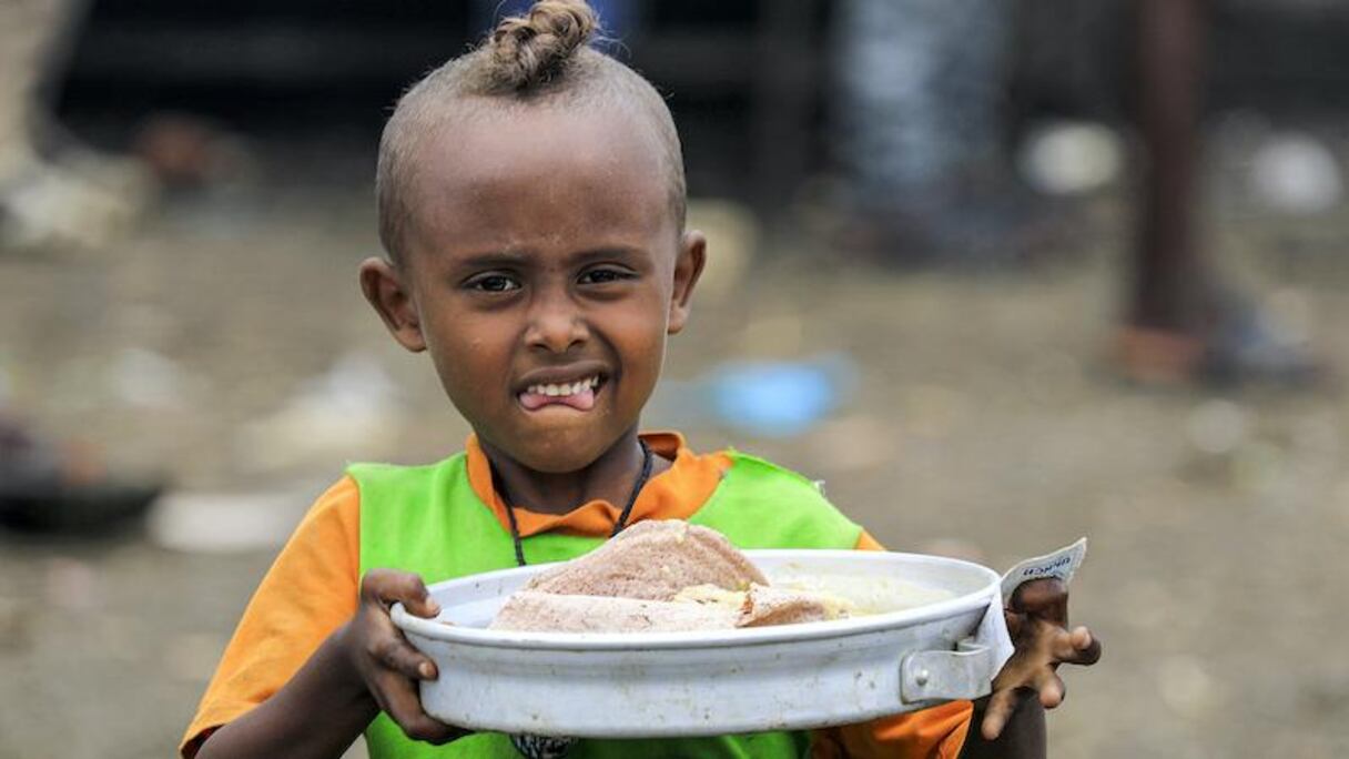 Un enfant réfugié au Soudan portant un plat de soupe et la traditionnel injera éthiopienne.